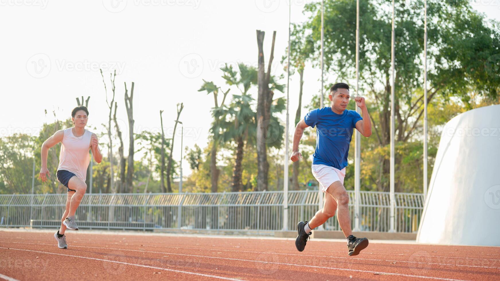 Blue shirt asian athlete man is running in front of a man in white tank top on the racetrack. photo