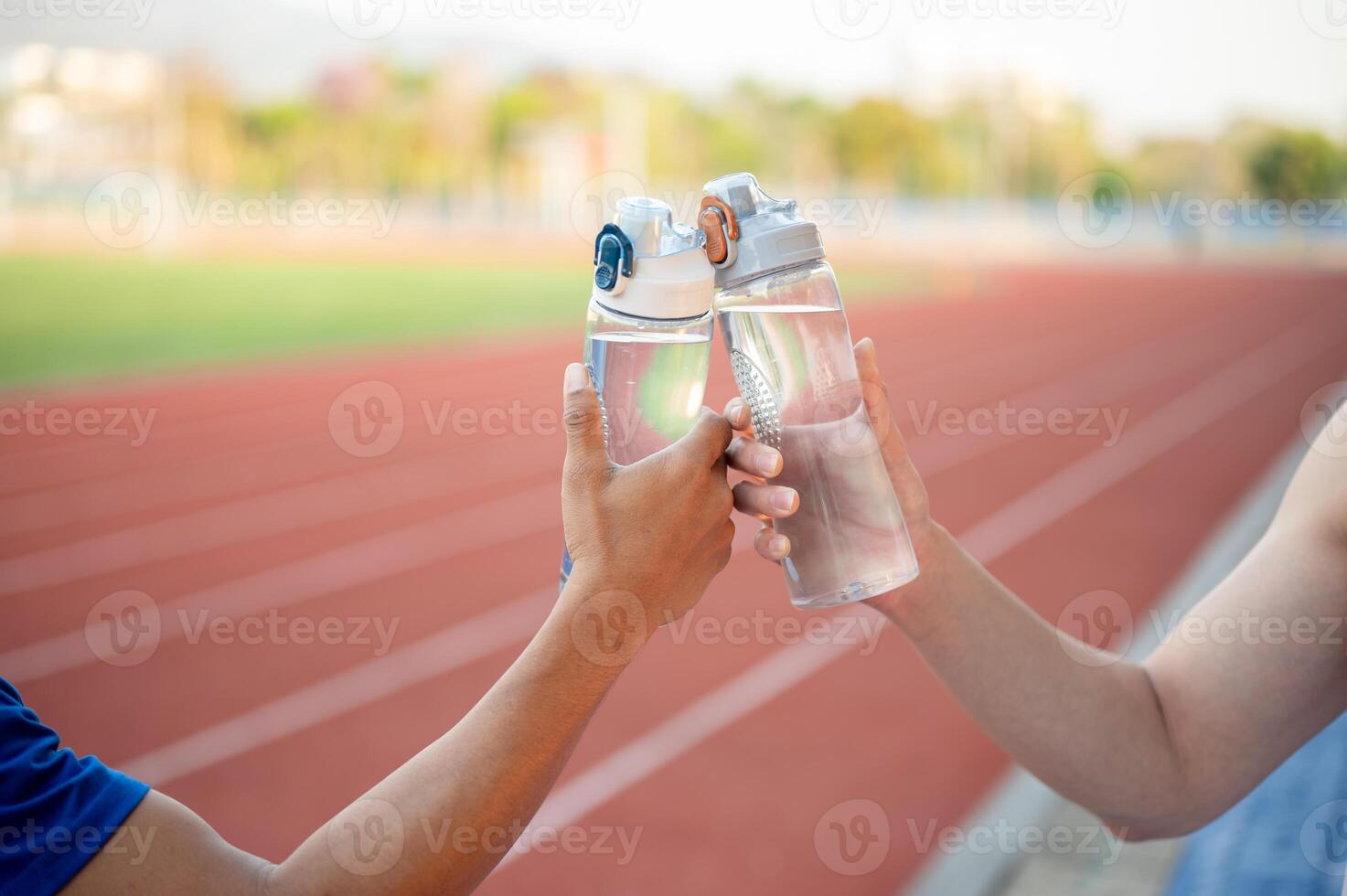 Two asian athlete men are holding and clinking their water bottles together on the racetrack. photo
