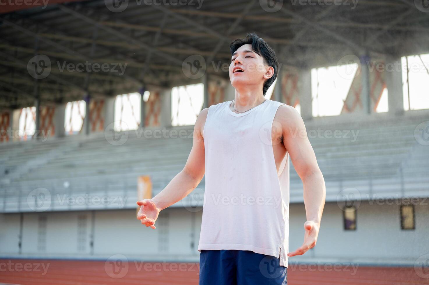 Asian man in white tank top standing with open arms and deep breathing, taking a rest after running. photo