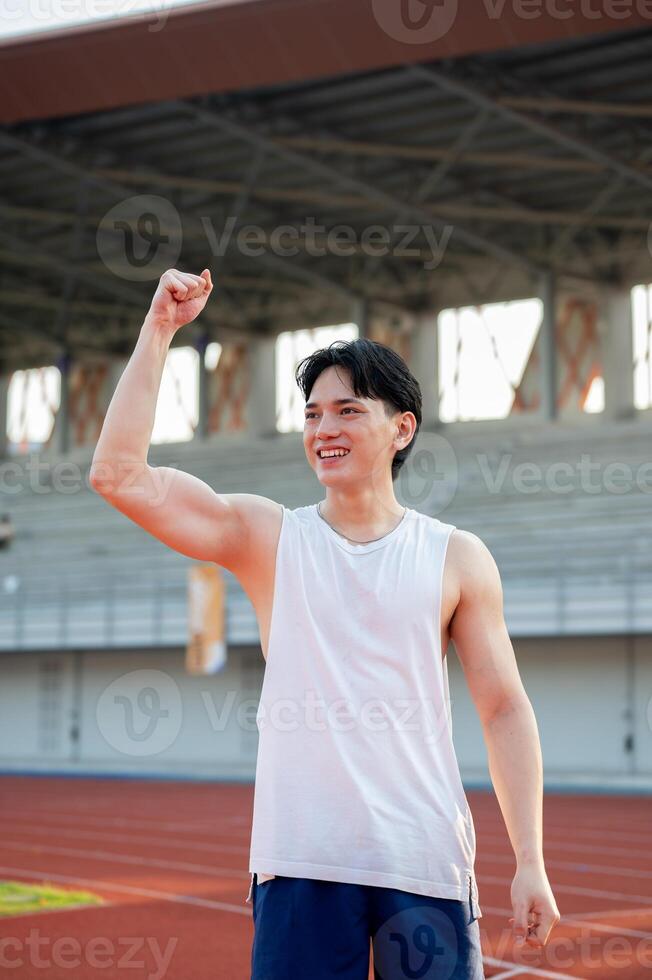 An asian man in white tank top is smiling and raising a fist while standing on the racetrack. photo