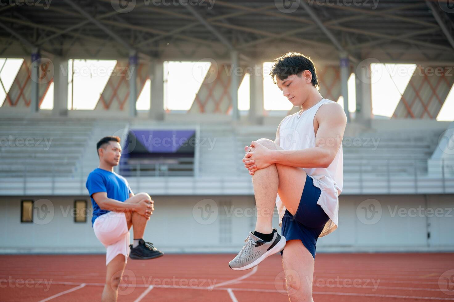 Two asian athlete men are stretching their legs muscles together on the racetrack. Outdoor exercise. photo