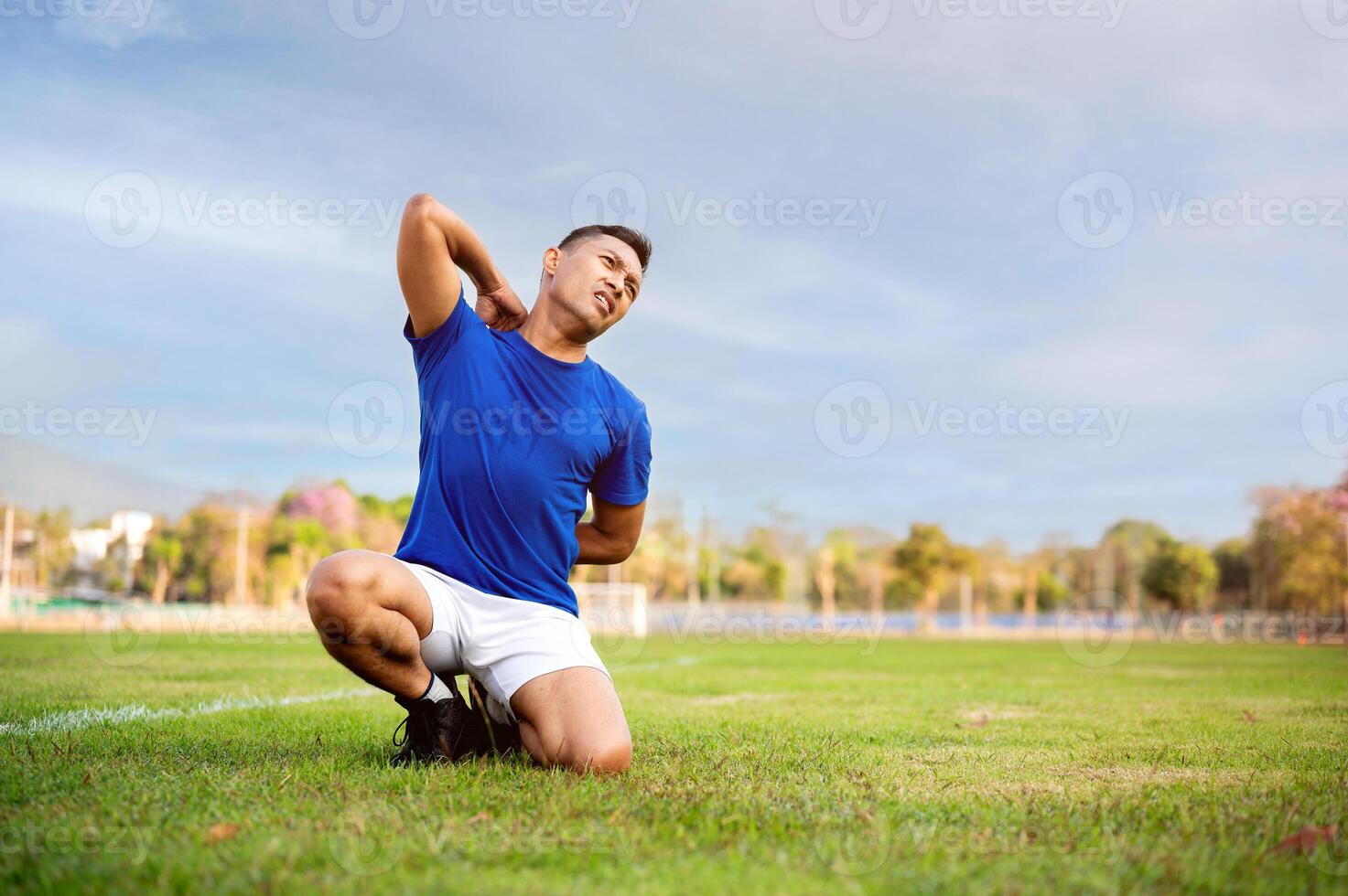 Asian man in blue t shirt is kneeling on grass and touching or massaging his back.Pain or injury. photo
