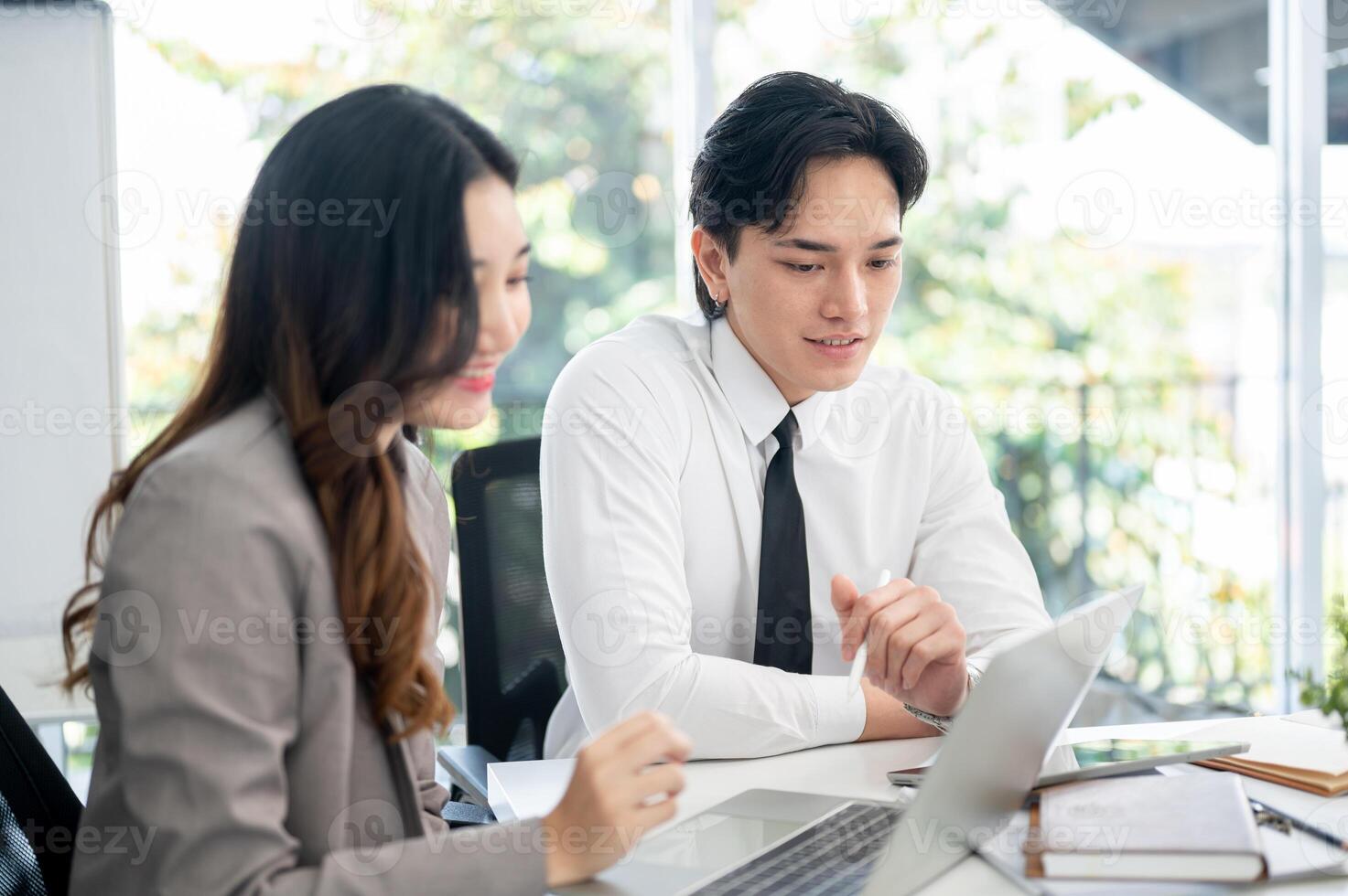 Female office worker and her male coworker is smiling while talking together at the working desk. photo