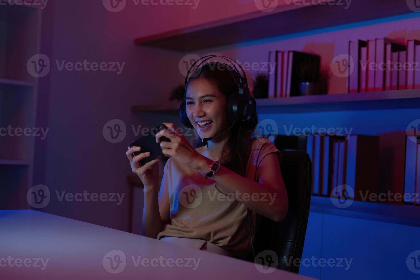 Gaming and Streaming. Joyful young woman playing mobile game with headset in colorful lighting. photo
