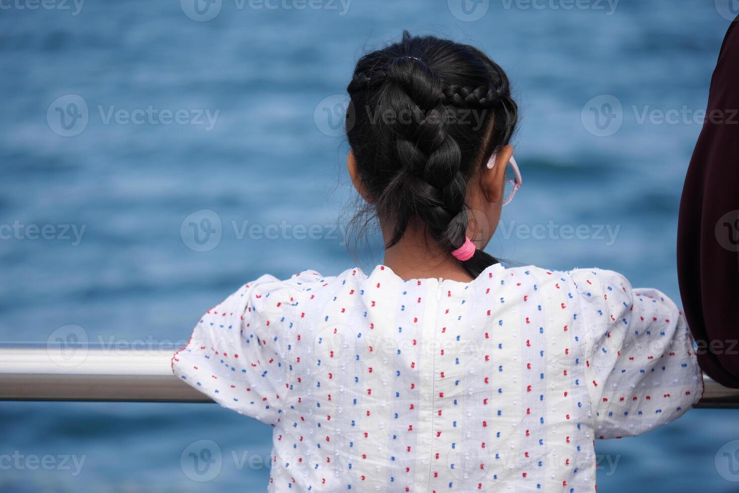 Child gazes over water while relaxing at the seaside photo