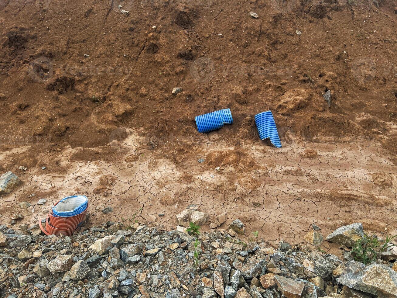 Blue drainage pipes and construction materials are scattered on dry, cracked earth, surrounded by rocky terrain, illustrating a construction site in a rural area with natural elements photo