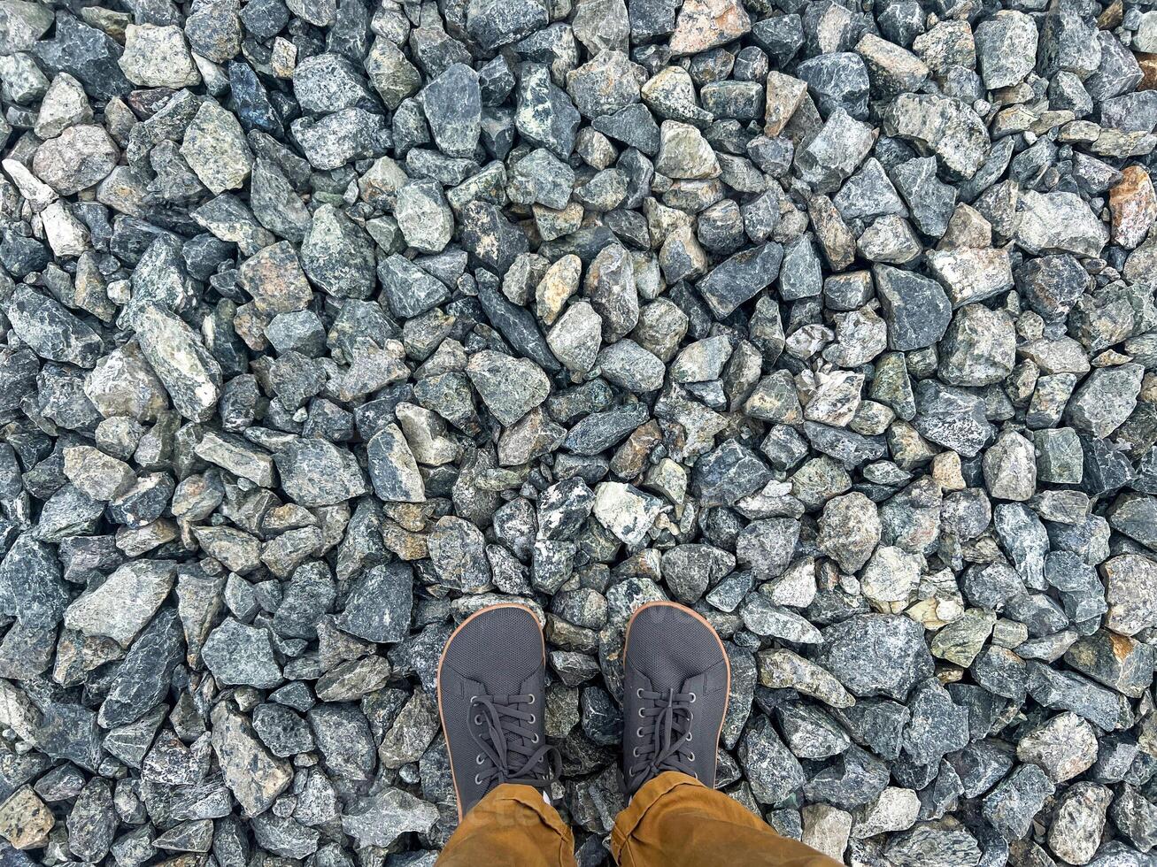 Person standing on a textured surface of small gray various sizes gravel stones, showcasing footwear and the natural patterns in a construction material setting , copy space photo