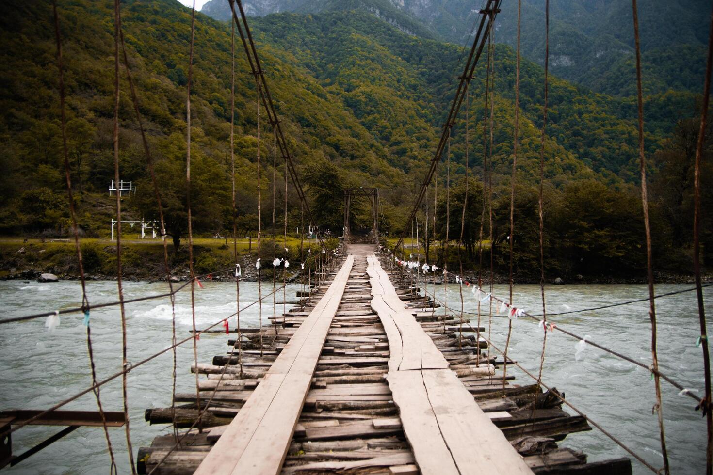 Rustic wooden footbridge over a rushing alpine river surrounded by rocks and forest photo