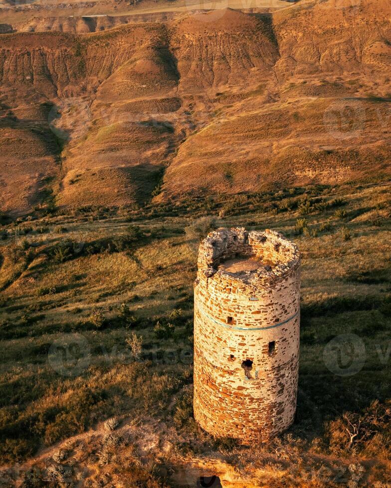 Aerial fly over view of an ancient stone watchtower standing alone on a remote ridge by David Gareja complex, Georgia, symbolizing medieval defense, isolation, and border vigilance. photo
