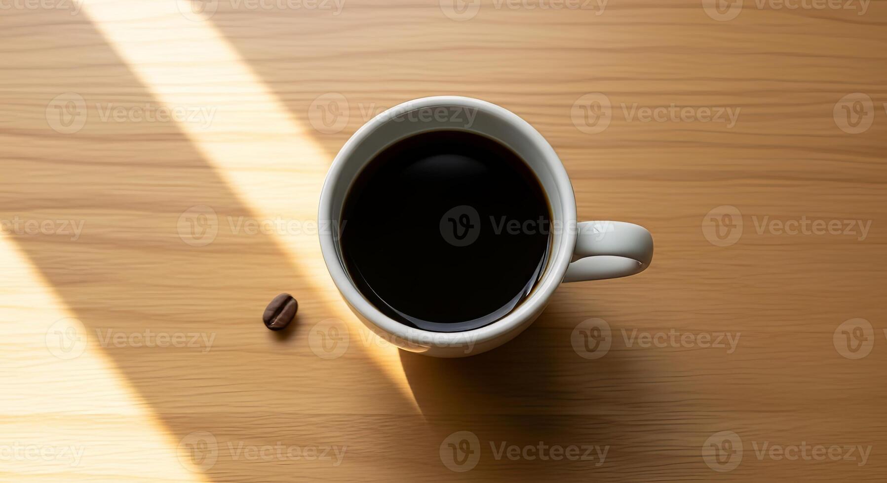 A cup of dark coffee sits on a wooden table in sunlight, a single coffee bean rests nearby photo