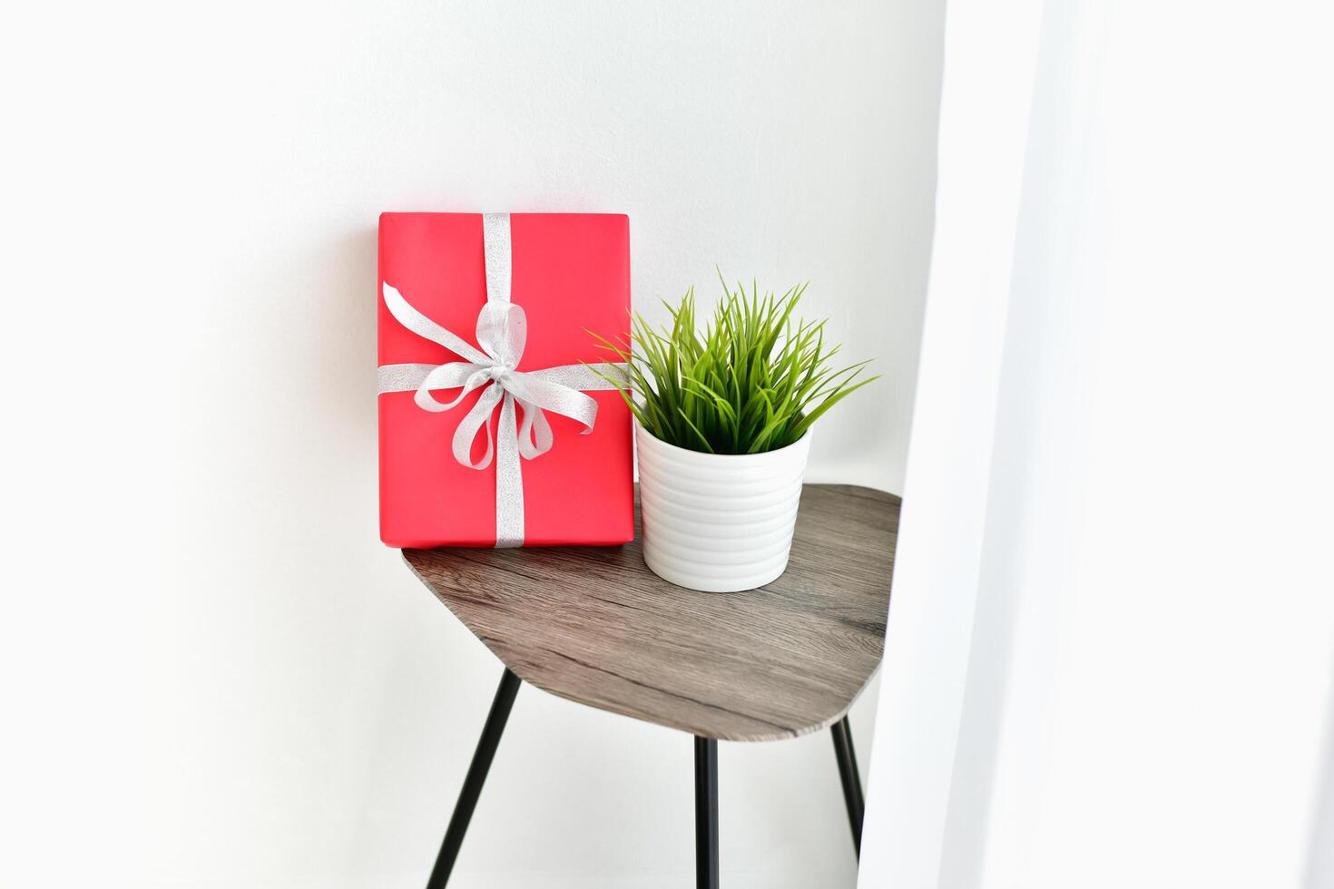 A red gift box sits on a small table next to a plant photo