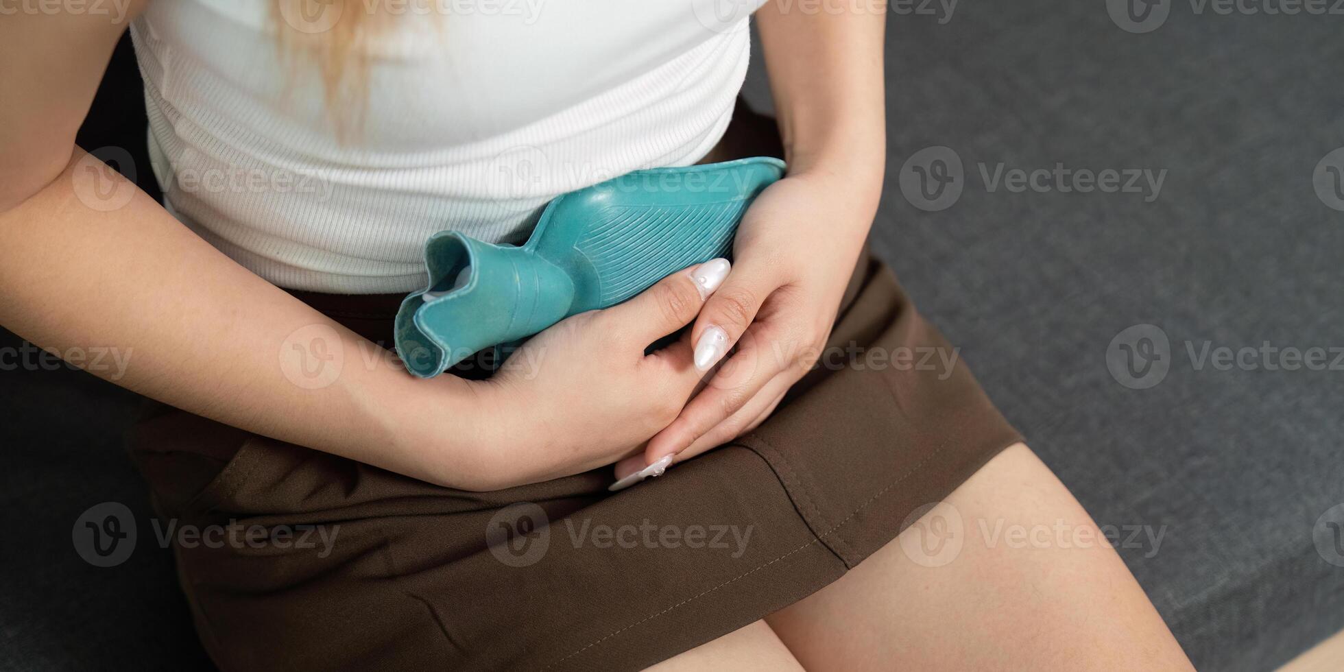 Comfort. Young woman using a hot water bottle for abdominal pain relief. photo