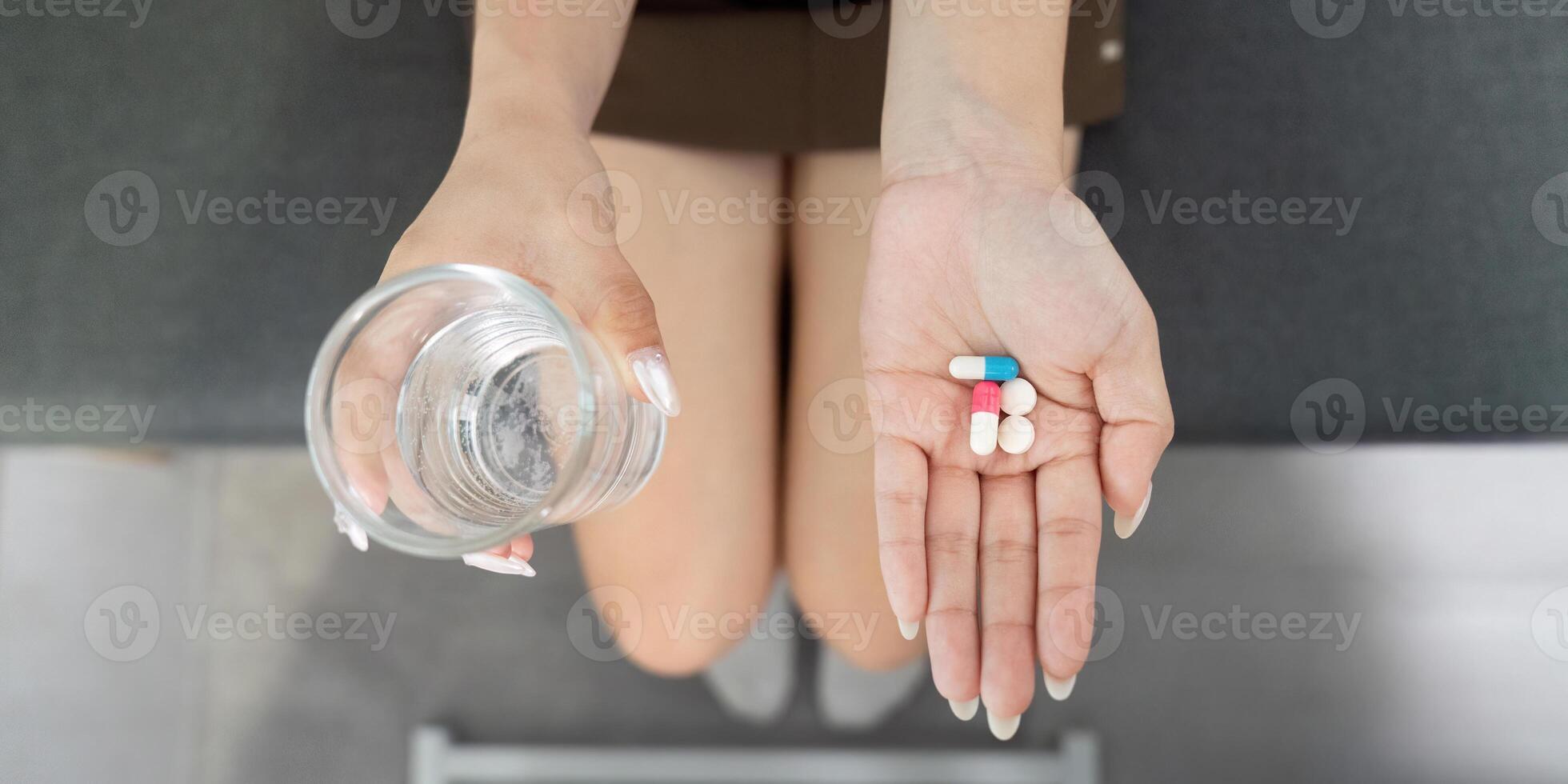 Medication. Young woman holding pills in one hand and a glass of water in the other. photo
