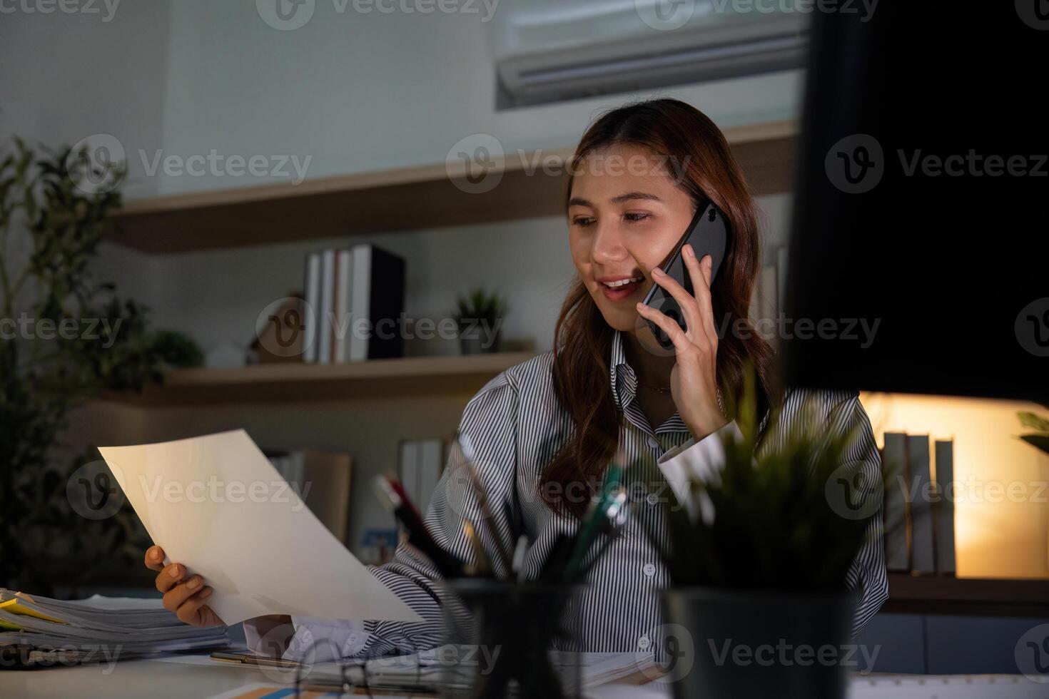 Late Night Work. Young professional on phone managing tasks in a dimly lit office. photo