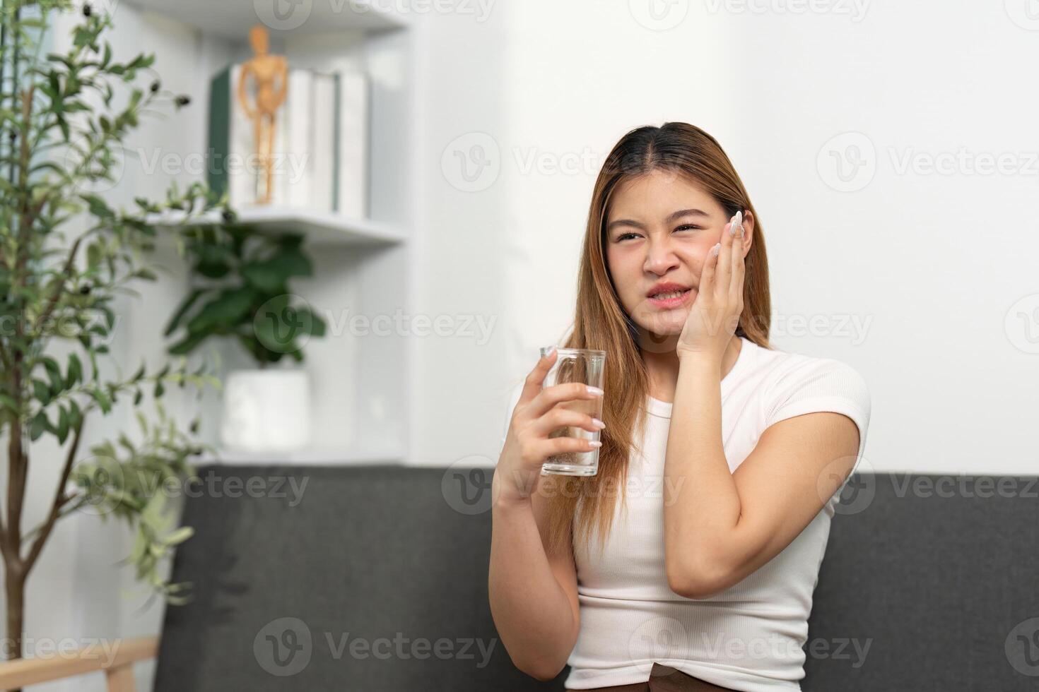 Health Awareness. Young woman holding a glass of water, showing discomfort. photo
