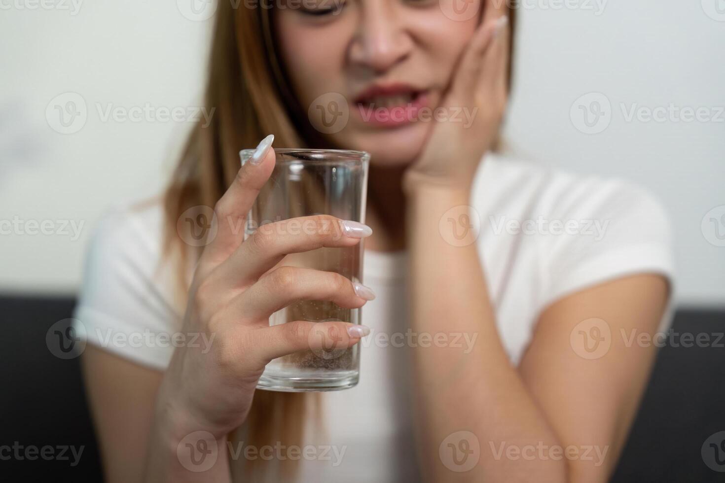Health Concern. Young woman experiencing dental pain while holding a glass of water. photo