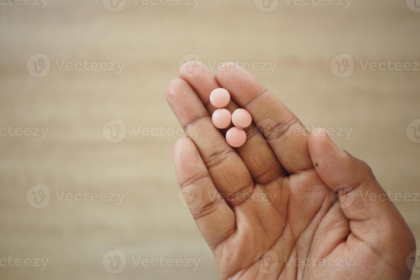 Hand holding four pink pills on a wooden surface photo