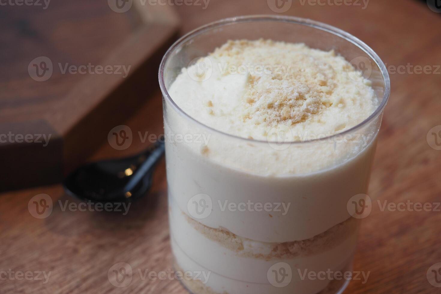 Creamy dessert in a clear cup on wooden table with spoon photo
