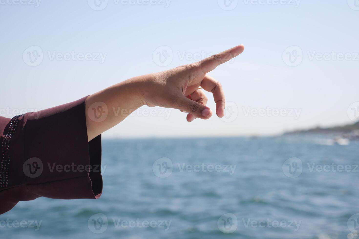 Hand pointing toward the horizon over tranquil water photo