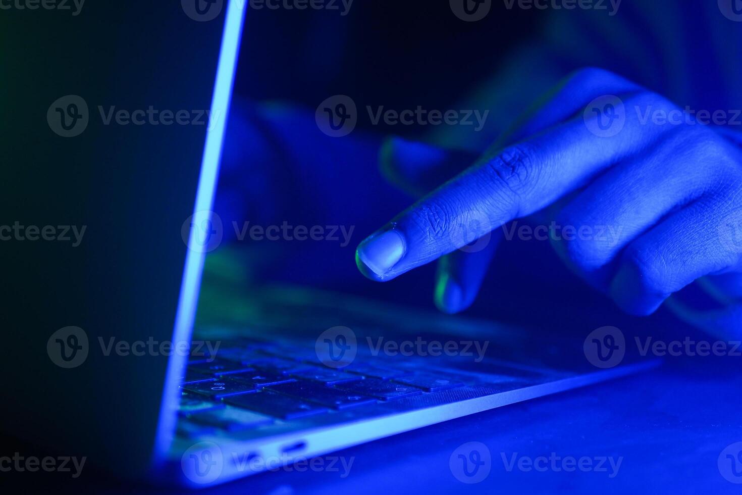 Hands engaged in typing on a laptop with blue lighting, cyber crime concept photo