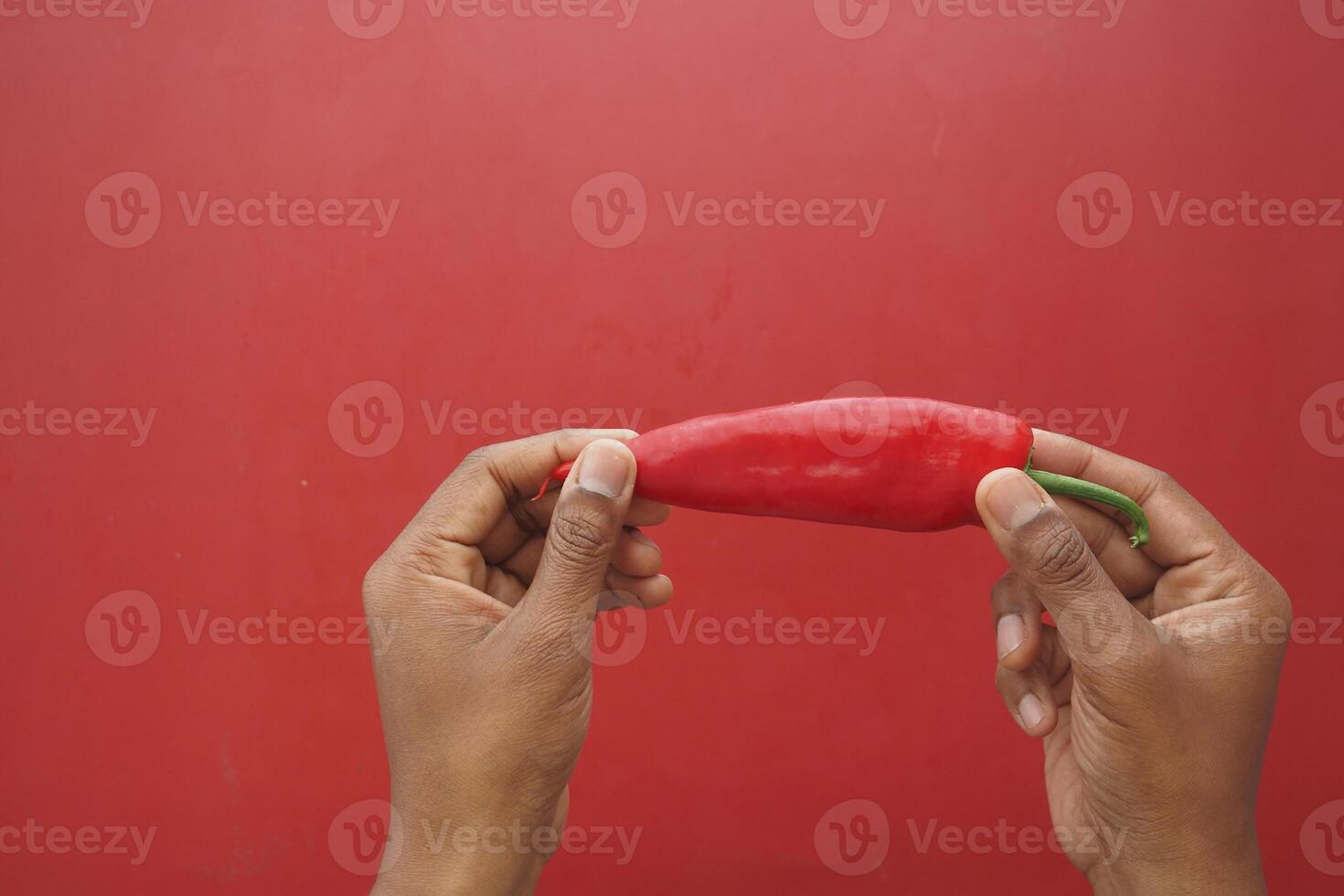 Hands holding a red chili pepper against a red background photo