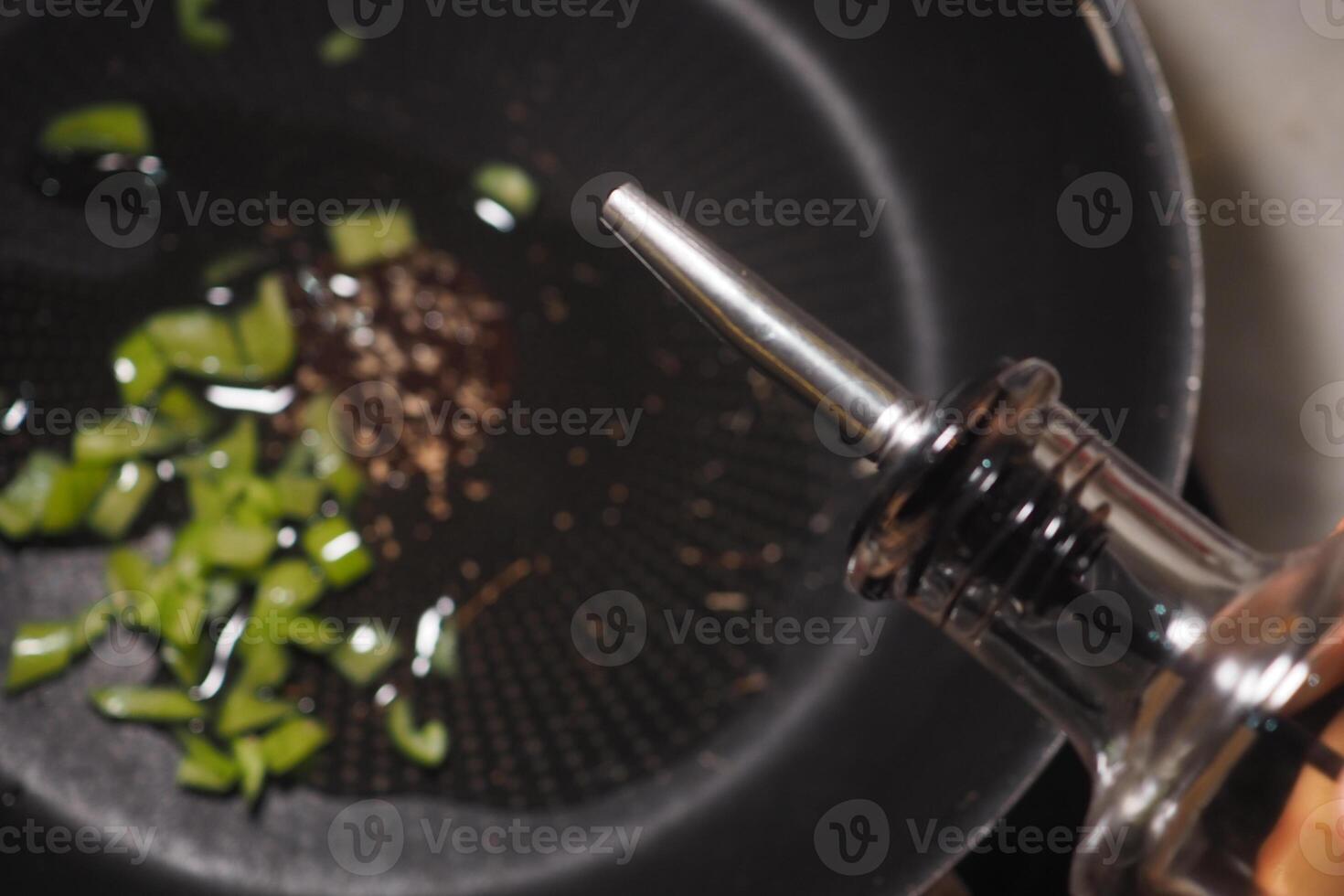 Cooking oil being drizzled over chopped herbs in skillet photo