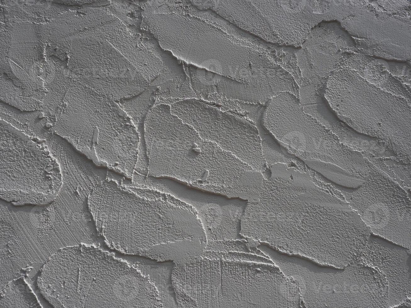 Textured wall surface with rough, uneven plaster finish showing cracks and ridges, creating rugged appearance with shadows highlighting depth and irregularities of material photo