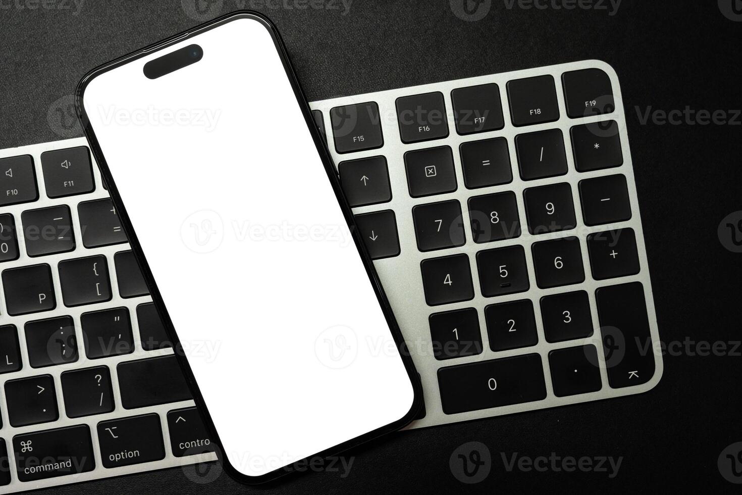 A modern smartphone with a blank white screen rests on a white and black computer keyboard, ideal for showcasing digital content or technology concepts. Copy space. photo