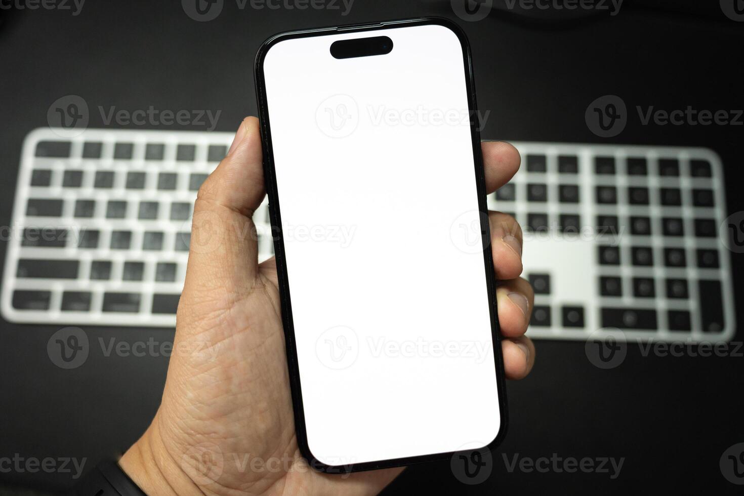 Hand Holding Blank Smartphone Over Keyboard. Perfect for showcasing mobile apps or web designs against a blurred keyboard background. photo