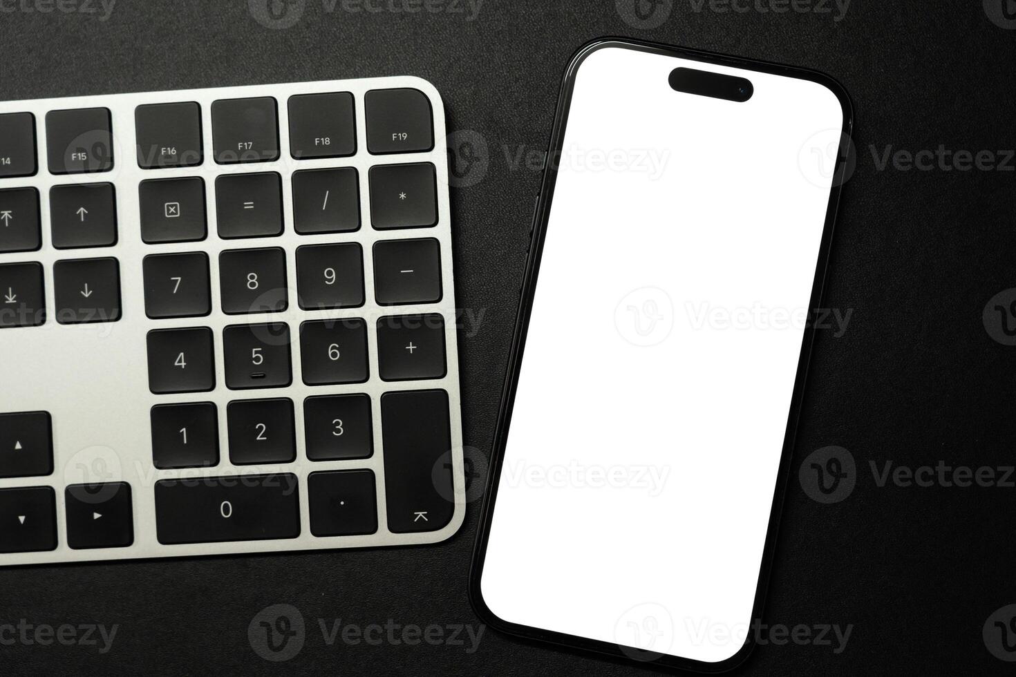 A modern smartphone with a blank white screen rests on a white and black computer keyboard, ideal for showcasing digital content or technology concepts. photo