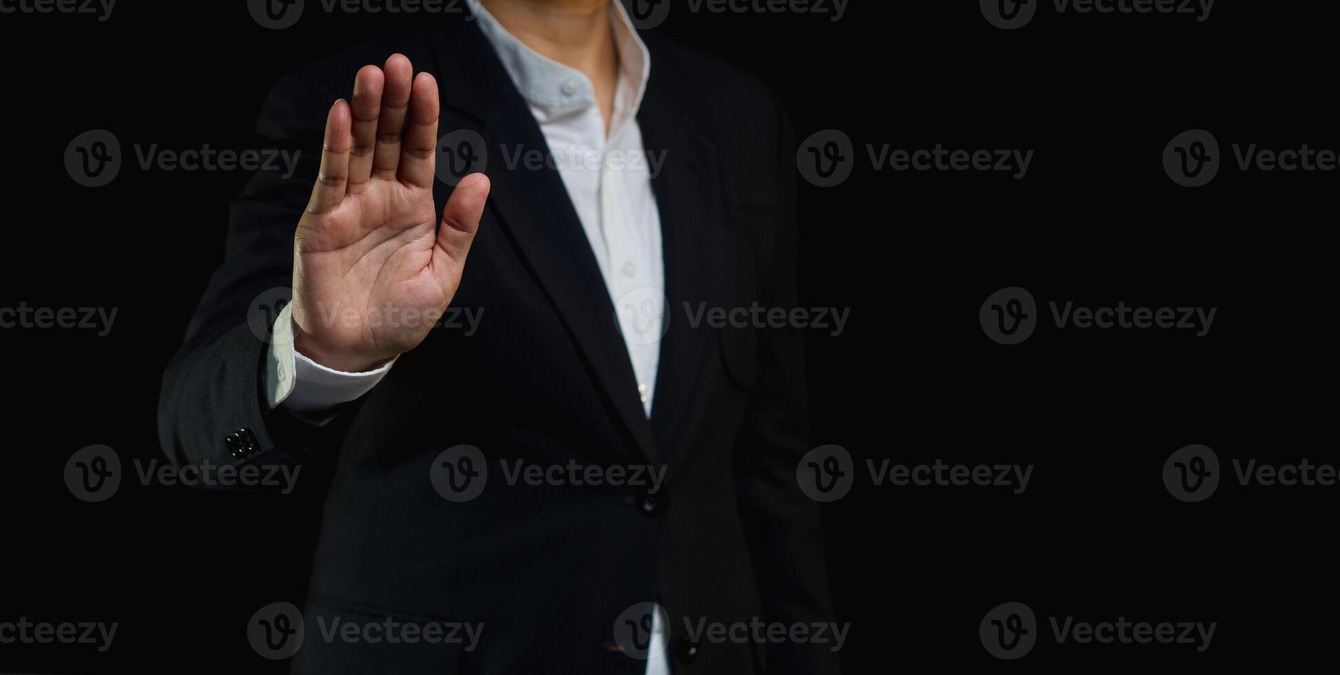 Businessman shows a stop gesture while standing on a black background. photo