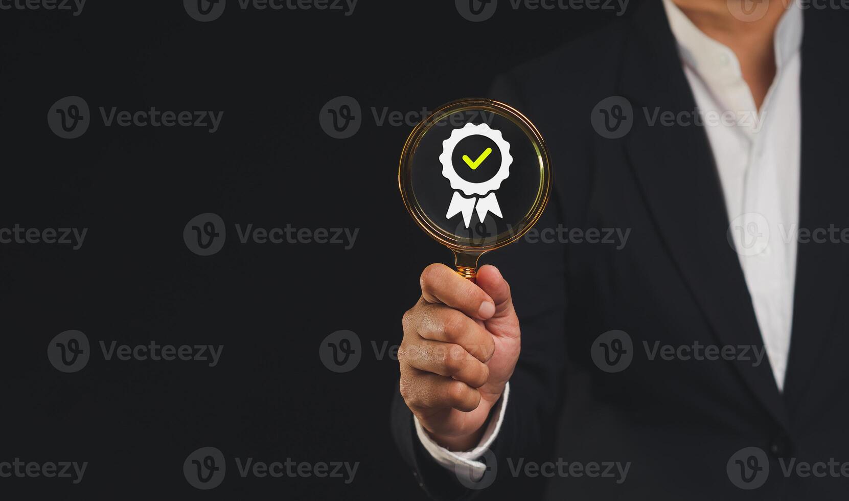 Businessman holding a magnifying glass with the best quality symbol assurance icon while standing against a black background photo