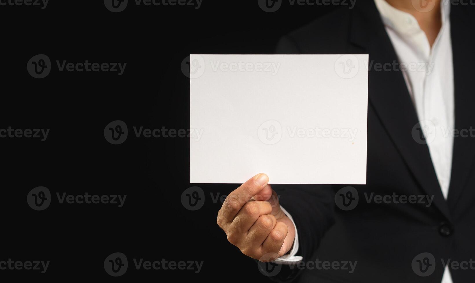 Businessman in a black suit holding a blank white paper while standing on a black background photo