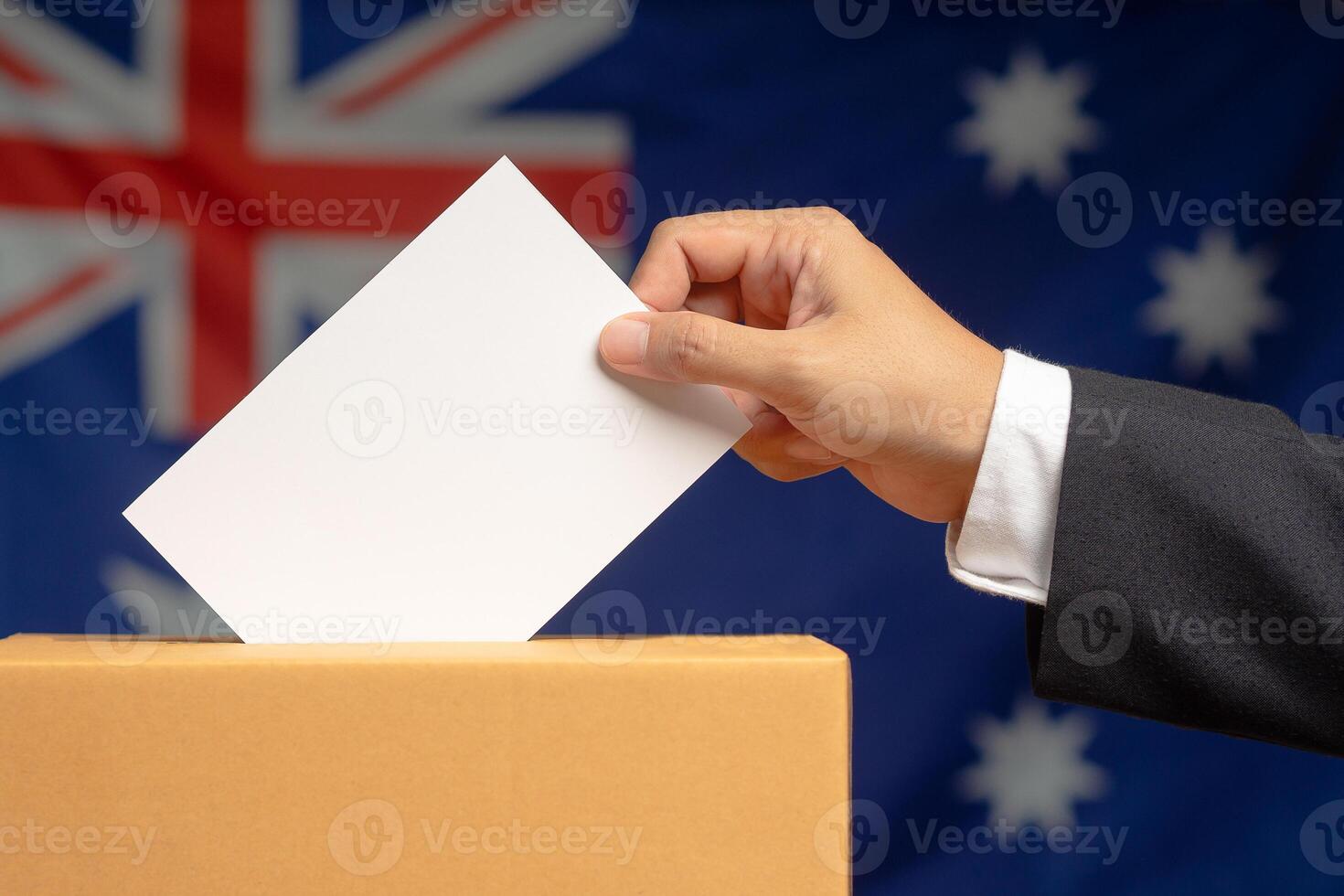 Hand voter holding ballot paper putting into the voting box at place election against the Australia flag background photo