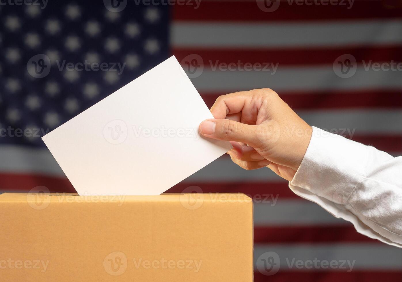 Close-up of a hand voter holding ballot paper putting into the voting box at place election against the American flag background photo