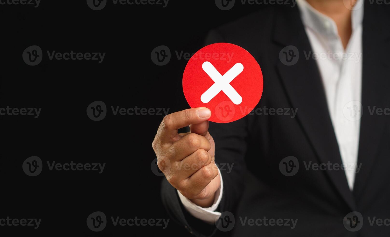 Businessman in a suit holding a cross symbol while standing on a black backgroun photo