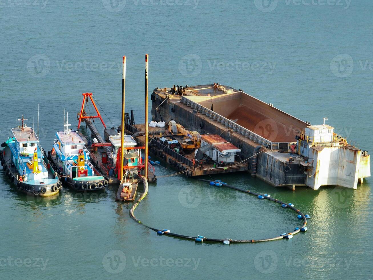 Heavy maritime engineering vessel conducting offshore dredging work with crane equipment and support boats in coastal waters for port deepening and marine construction infrastructure photo