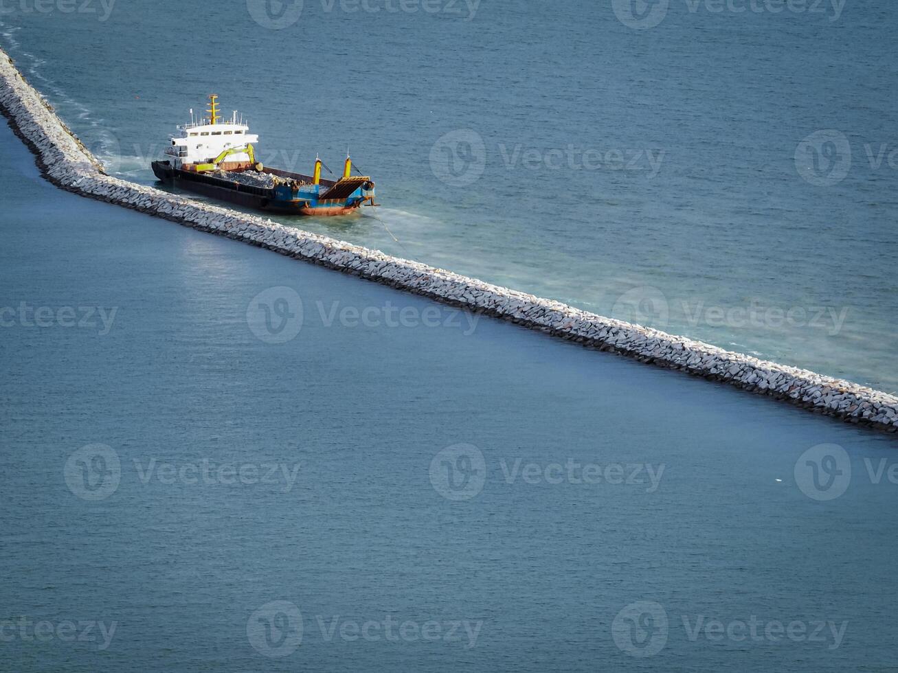 Marine construction vessel working on stone breakwater project in ocean. Coastal infrastructure development and harbor protection engineering work in progress. Port construction and coastal defense. photo