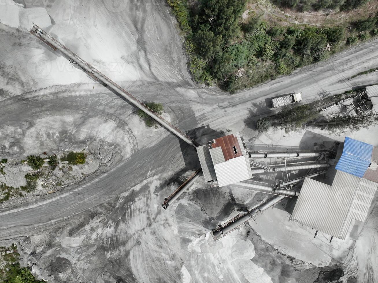 Aerial drone view of industrial stone crushing plant with conveyor belts and truck at limestone processing facility surrounded by forest, showing heavy equipment infrastructure and quarry operations. photo