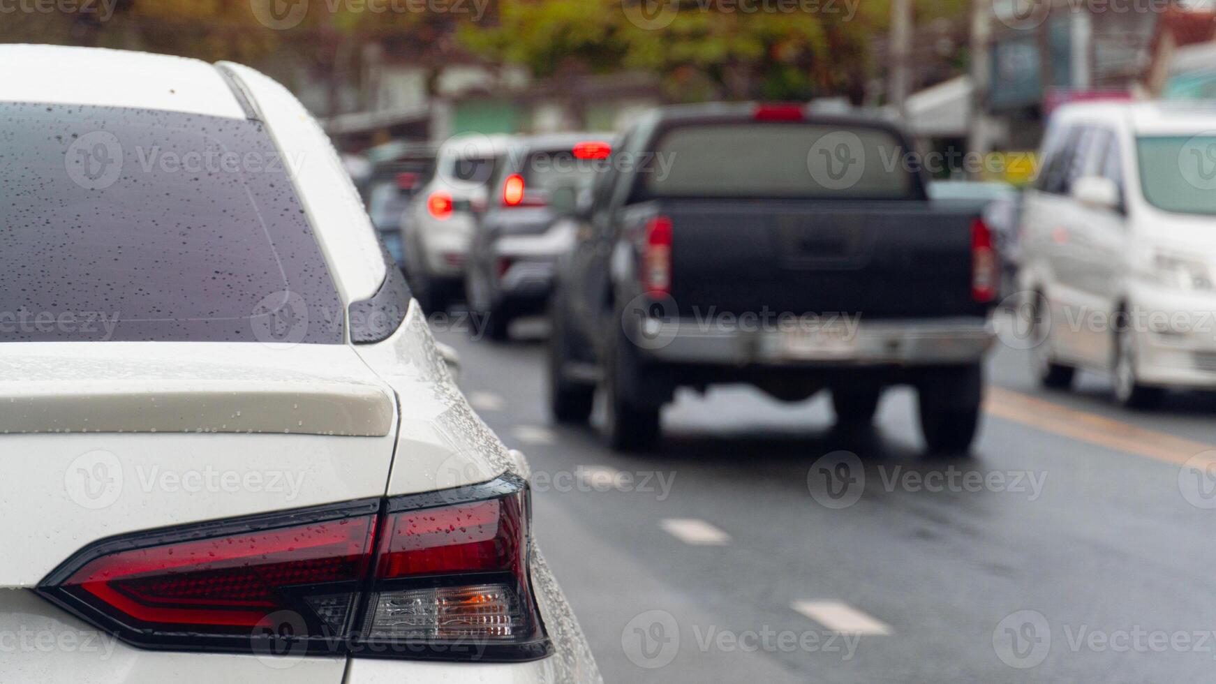 Rear side of white car stop on the wet road. Traffic on the road in rainy time. on the body of car wet drop of rain. Traffic jam in the city after rainy time. Side of road with many cars. photo