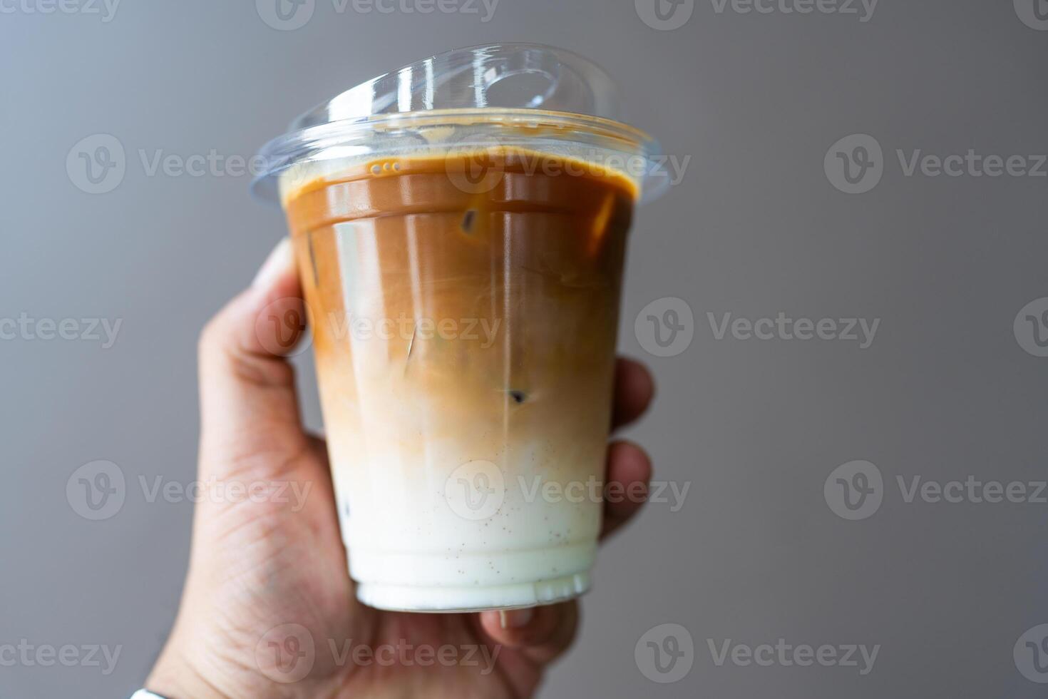 Someone hand holding a cup of iced latte, showing two coffee and fresh milk layer photo