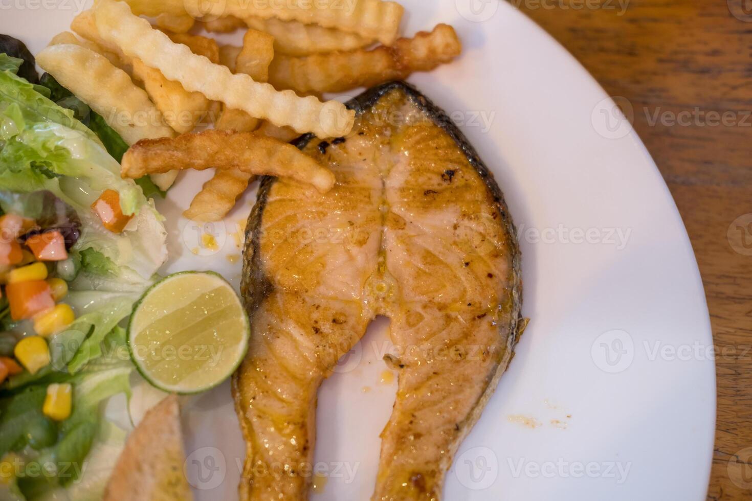 Grilled salmon steak slices served with salad and french fries photo