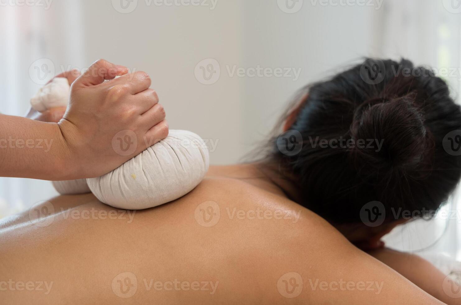 Thai herbal compress massage treatment. Therapist applying white cloth herbal compress on woman back at spa salon or wellness center photo