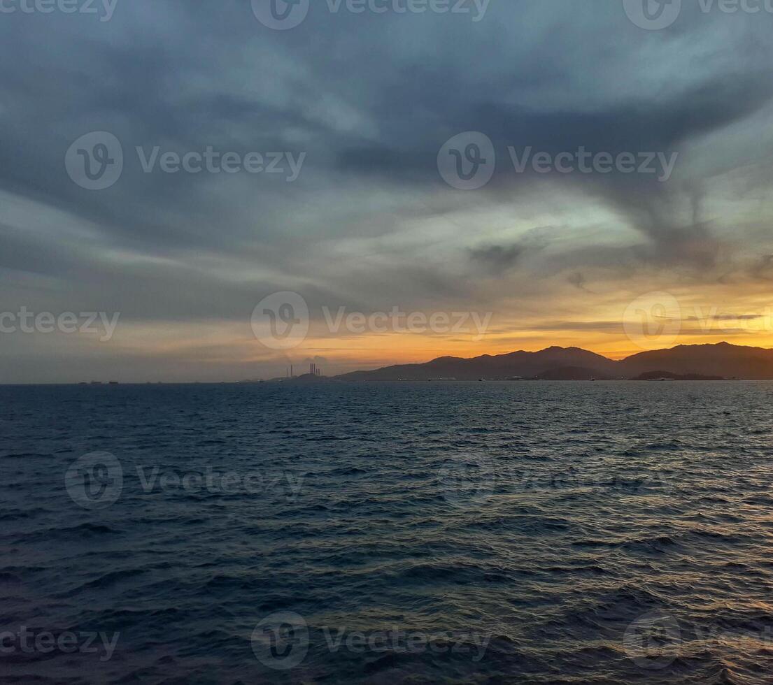 Dramatic Sunset Over Tranquil Ocean with Distant Mountains and Industrial Silhouette photo