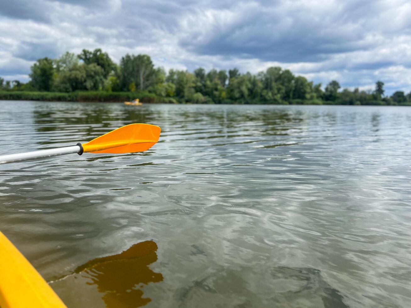 Yellow kayak paddle gliding through calm lake water under cloudy sky photo