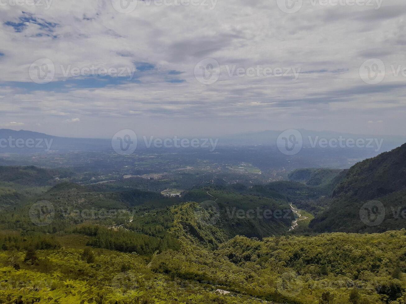 Expansive Mountain Vista Lush Green Valleys, Misty Distant City, Cloudy Sky. photo