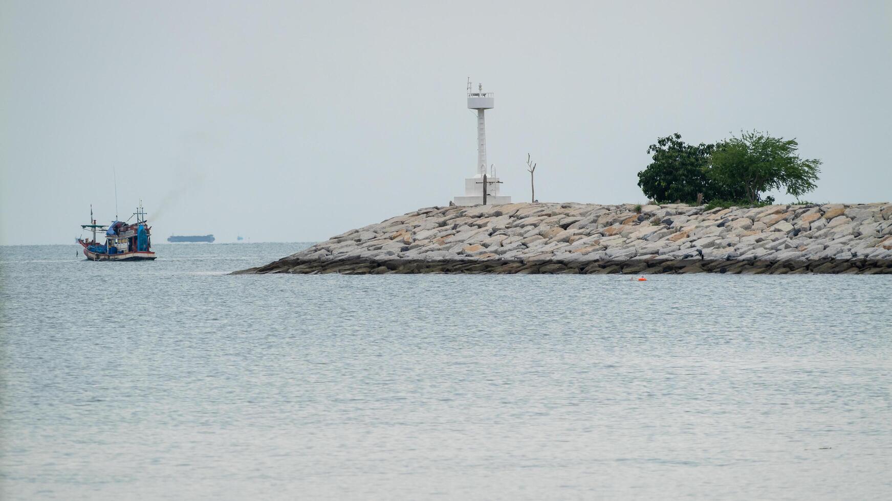 Fishing boat anchored by lighthouse at coastal jetty tranquil waters serene atmosphere wide angle view photo
