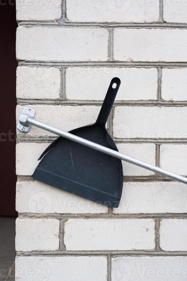 Plastic, black dustpan was stuck between the railing and the wall of the house photo