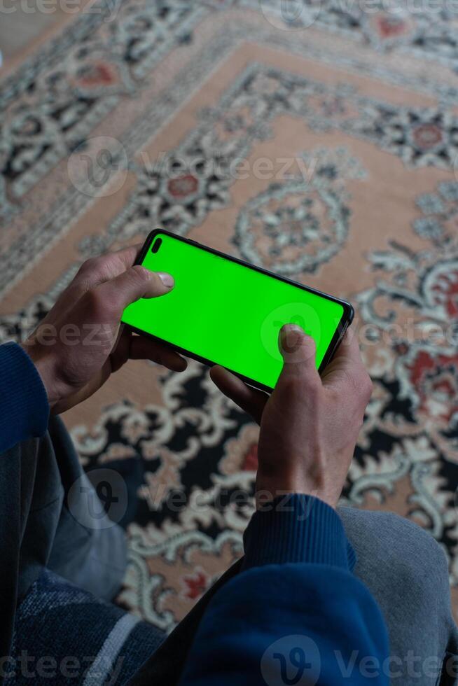 Guy is sitting with a smartphone in his hands with the green screen turned on photo