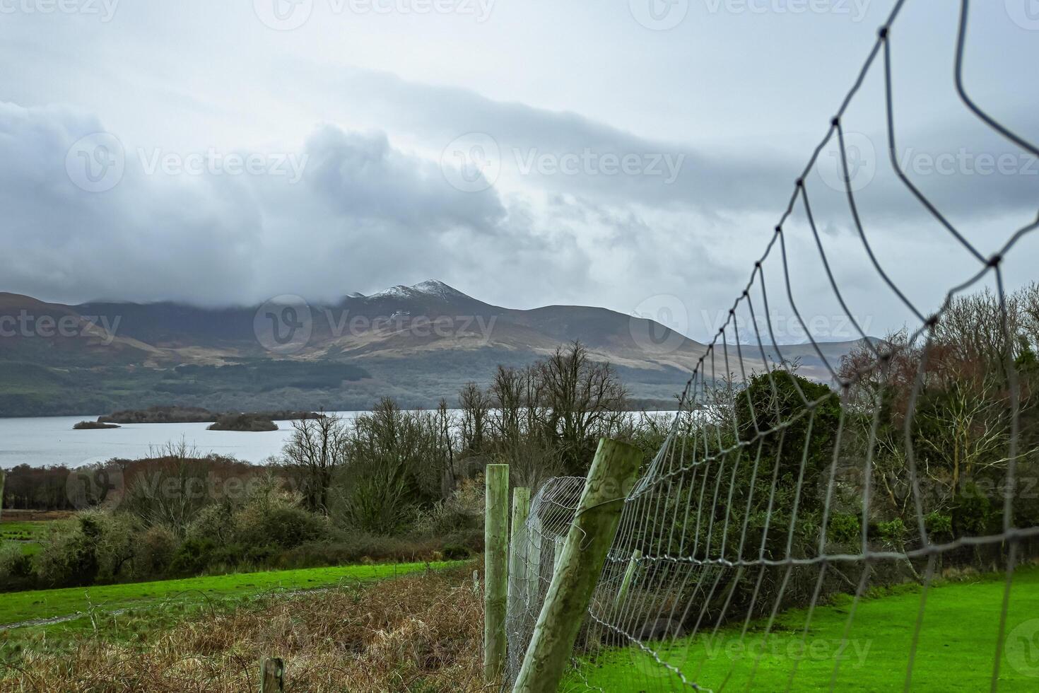 A fence encloses a grassy field with mountains behind it photo